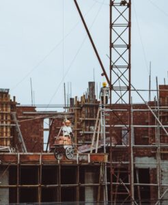 A construction worker on a scaffold at a building site with cranes and brickwork visible.