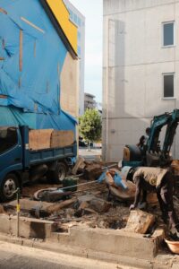 City construction site featuring workers, machinery, and a blue tarped building.